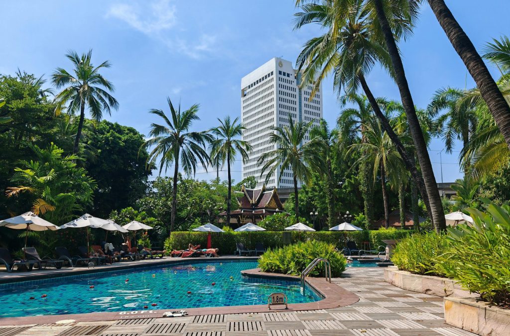 Luxurious tropical poolside setting with a city skyline view on a sunny day.